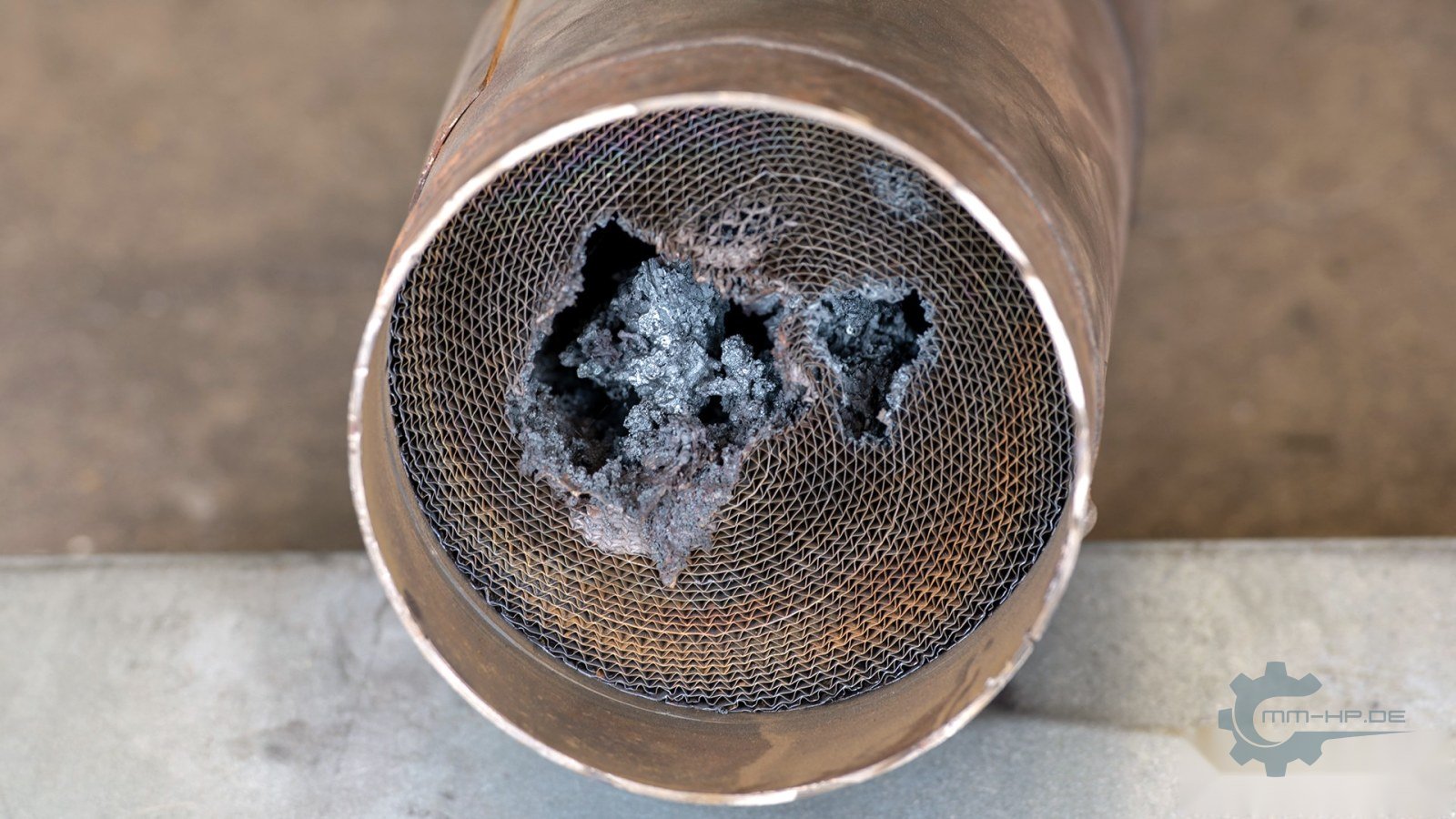Durchgeschmolzener Metallträger eines Katalysators, die Wabenstruktur ist in der Mitte zusammengelaufen
