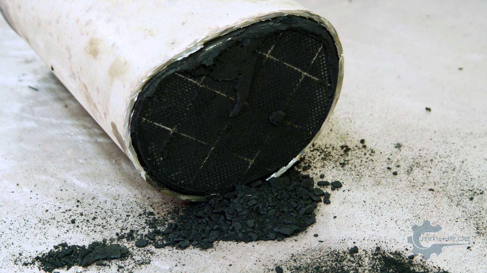Front face of a removed particulate filter overloaded with soot, the soot cake breaking off in places, the bonding joints between the segments visible as lines