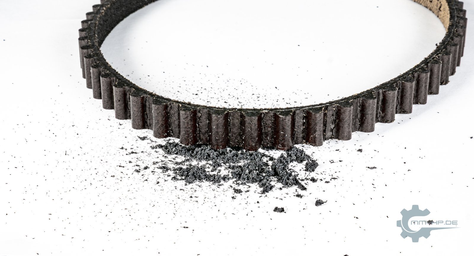 Used toothed belt with a small pile of black debris in front of it