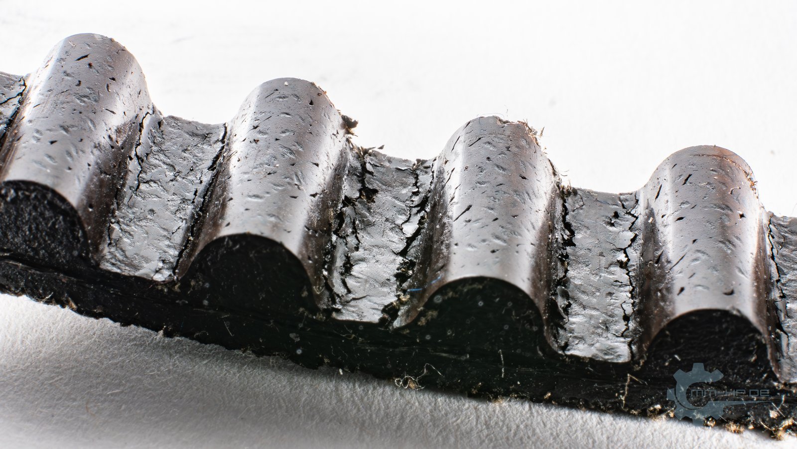 Close-up of toothed-belt teeth with a swollen, cracked surface